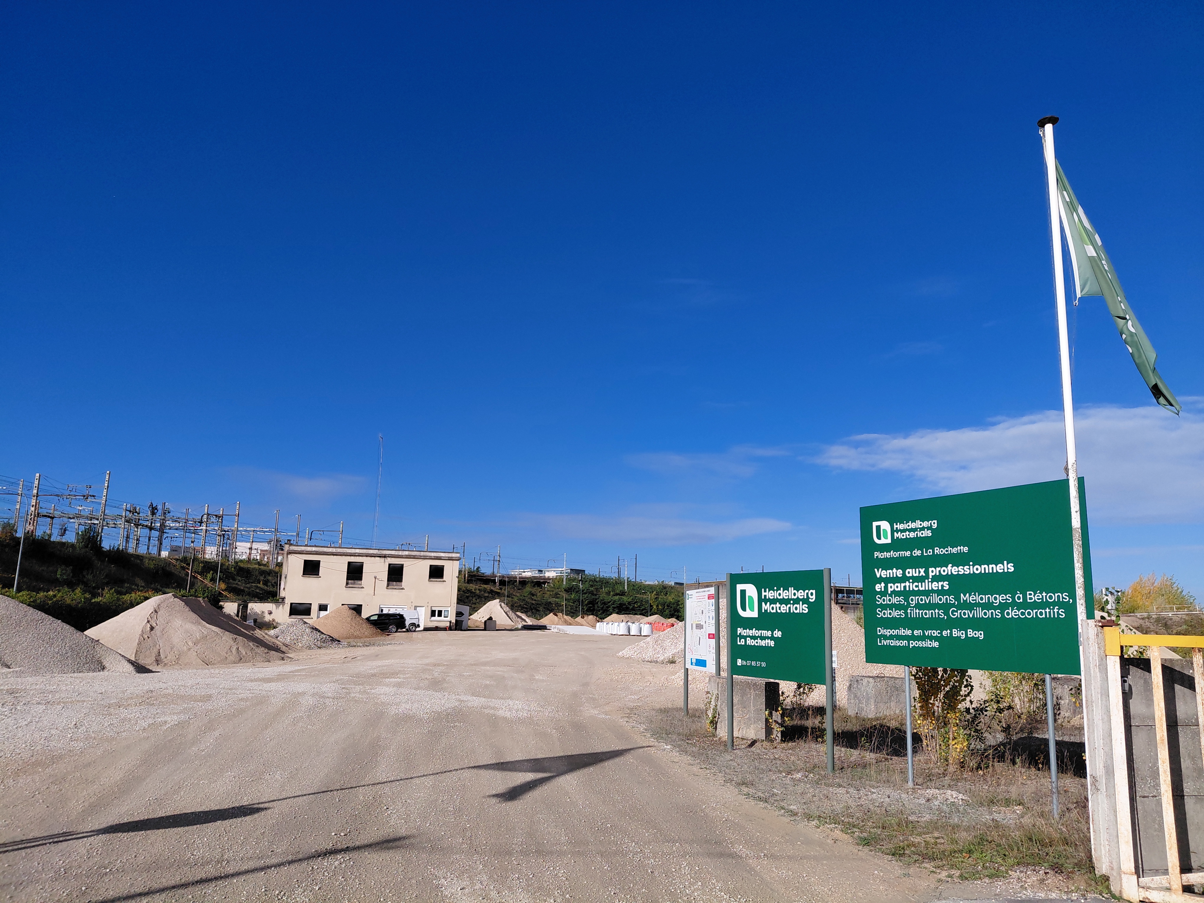 Entrée d'une carrière de granulats avec panneaux signalétiques et piles de matériaux visibles.