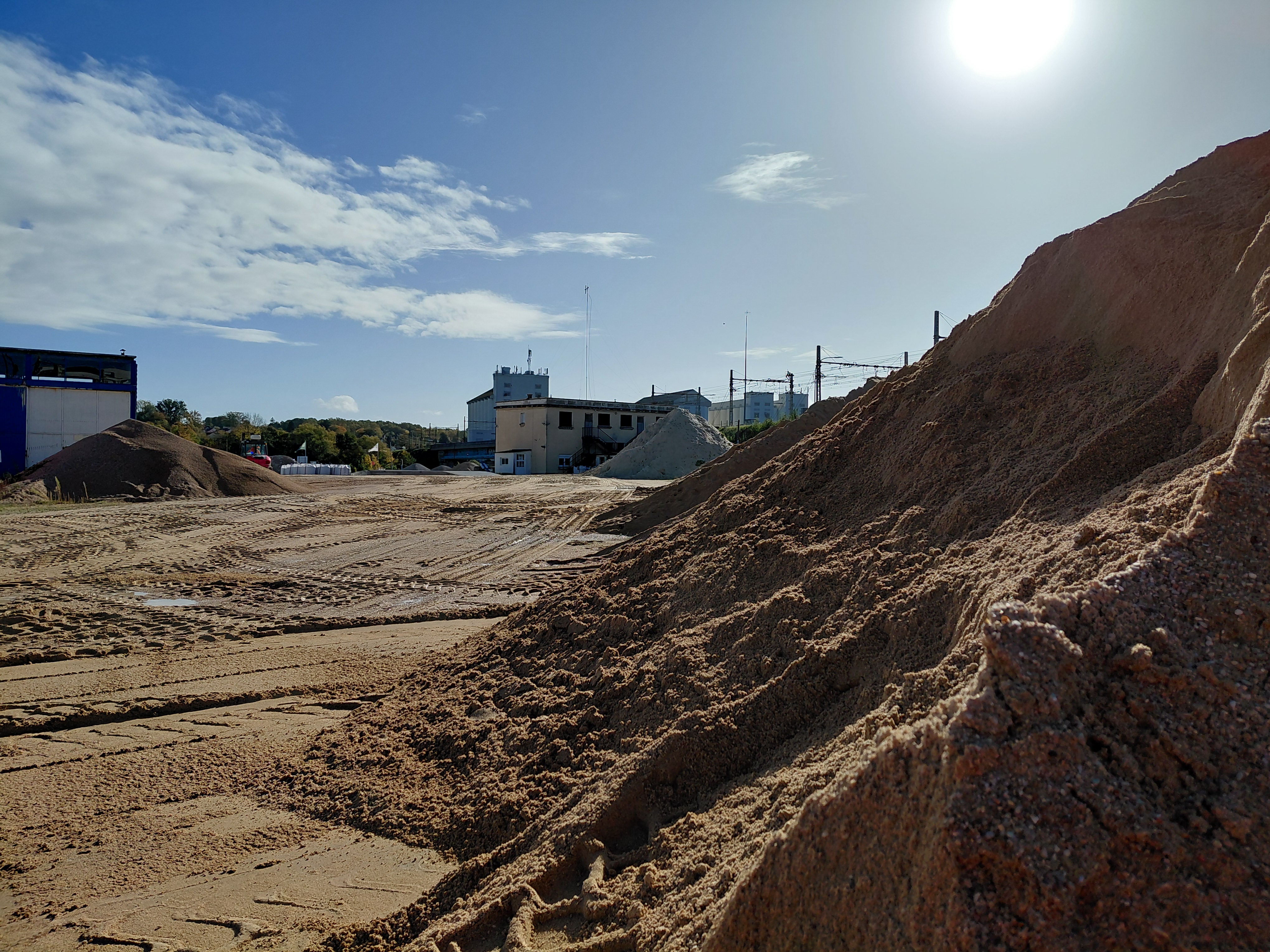 Stock de sable et infrastructures d'une carrière de granulats sous un ciel ensoleillé.