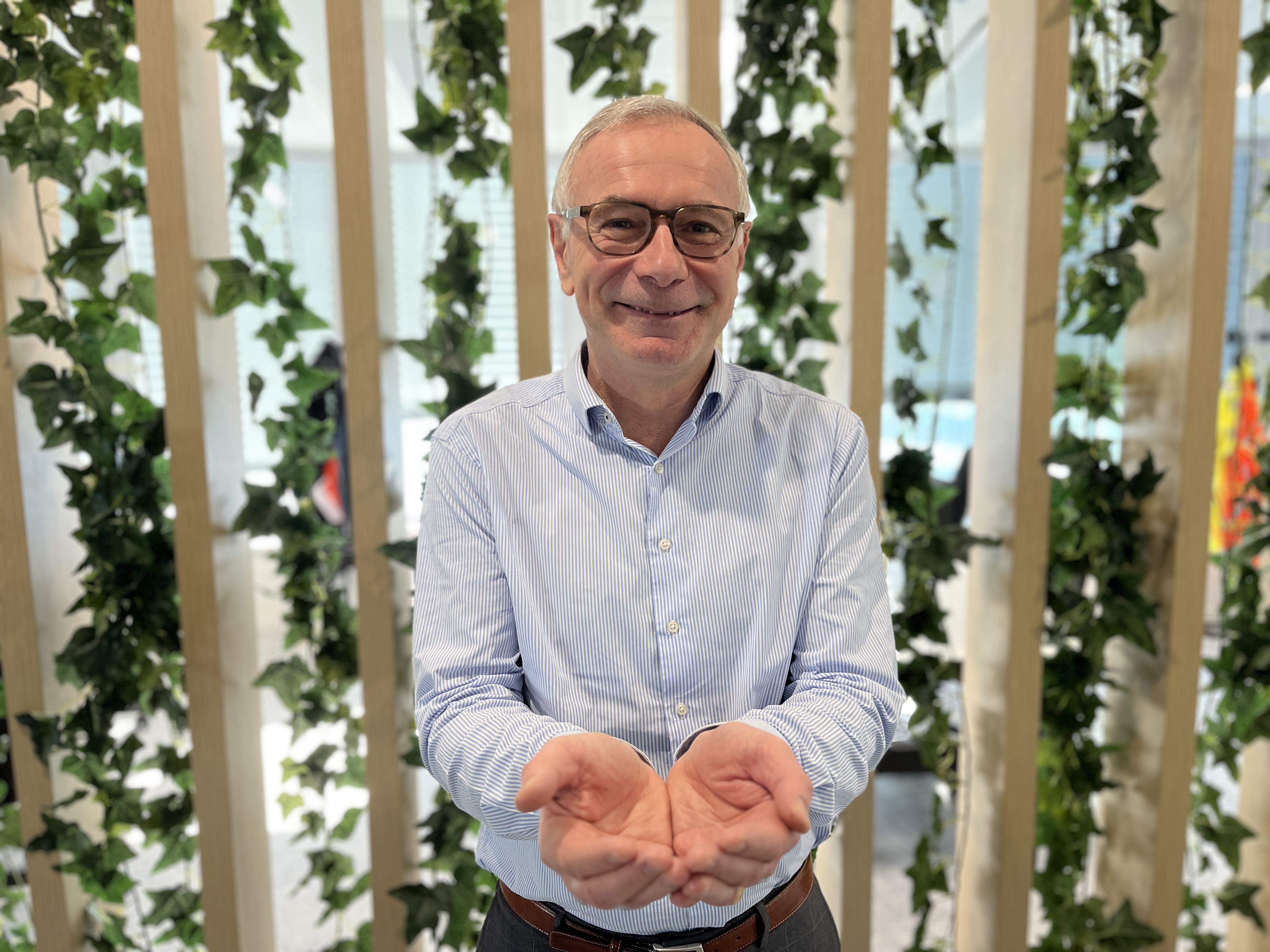 Personne en tenue professionnelle, les mains ouvertes, debout près d'une végétation.