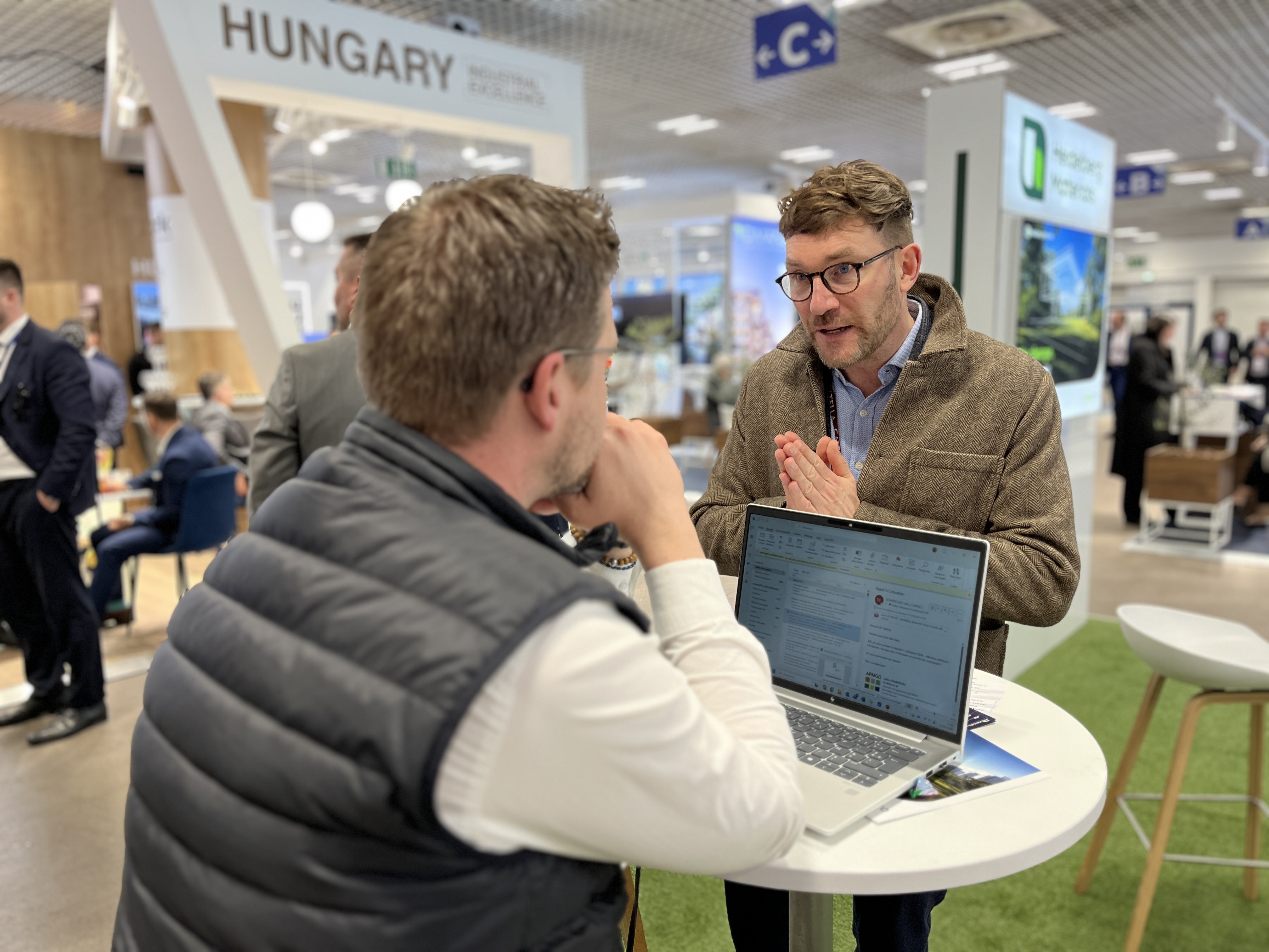 Deux personnes discutent devant un ordinateur portable sur une table dans un salon professionnel lié à la construction.