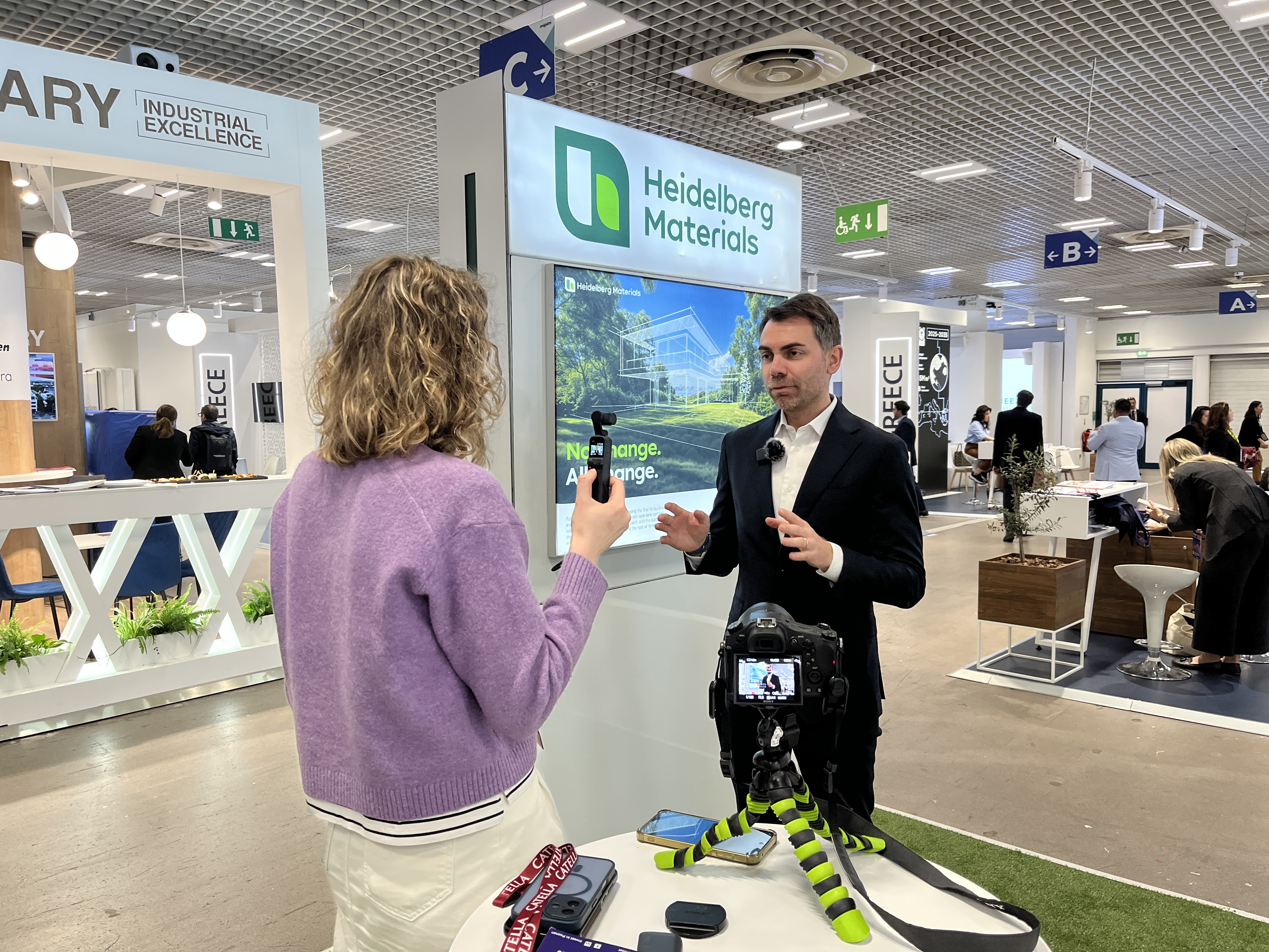 Une personne interviewe un homme devant un stand de Heidelberg Materials dans un espace d'exposition.