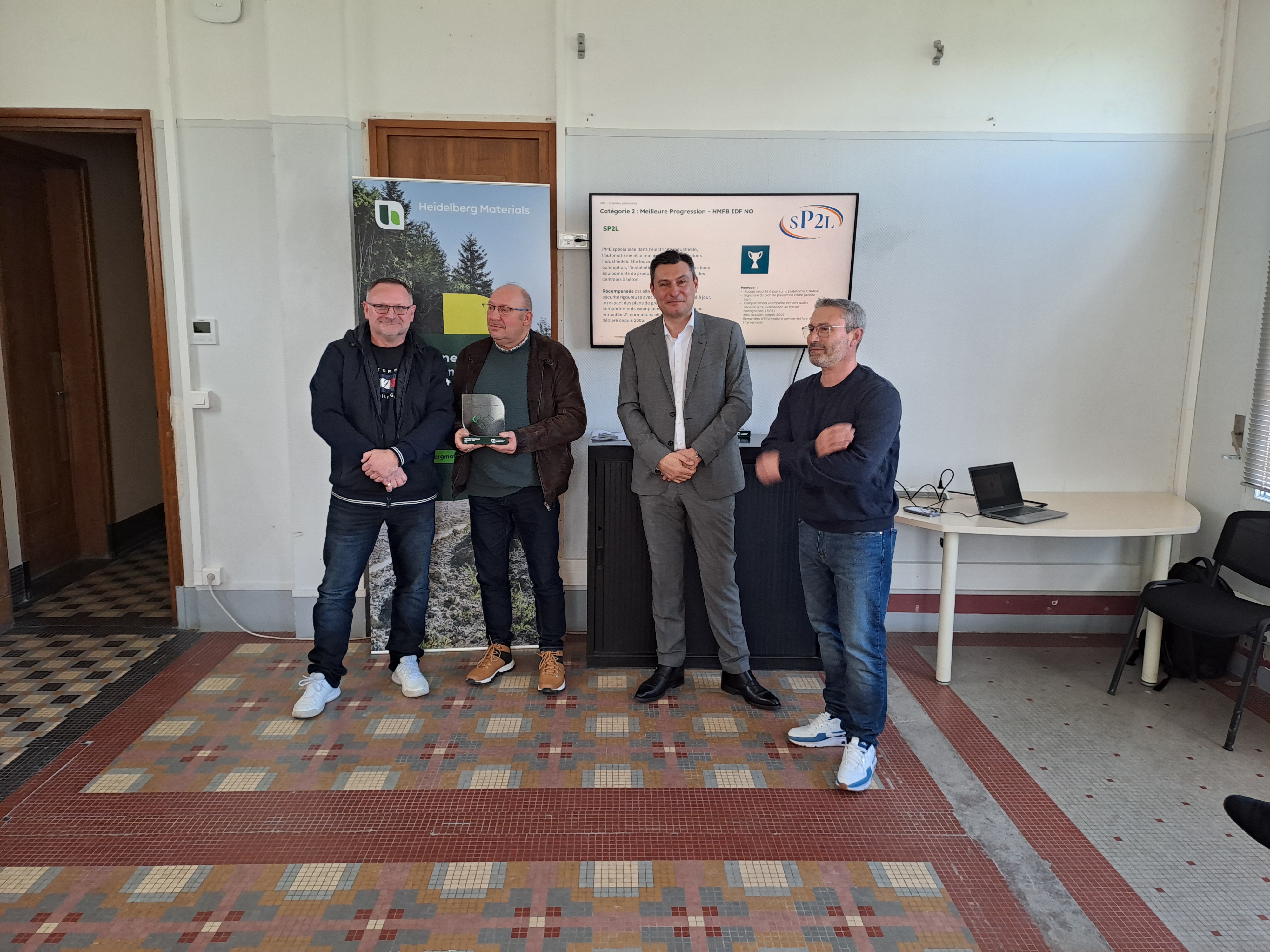 Des hommes posent debout dans une salle, un écran affichant des informations sur Heidelberg Materials est visible à l'arrière-plan.
