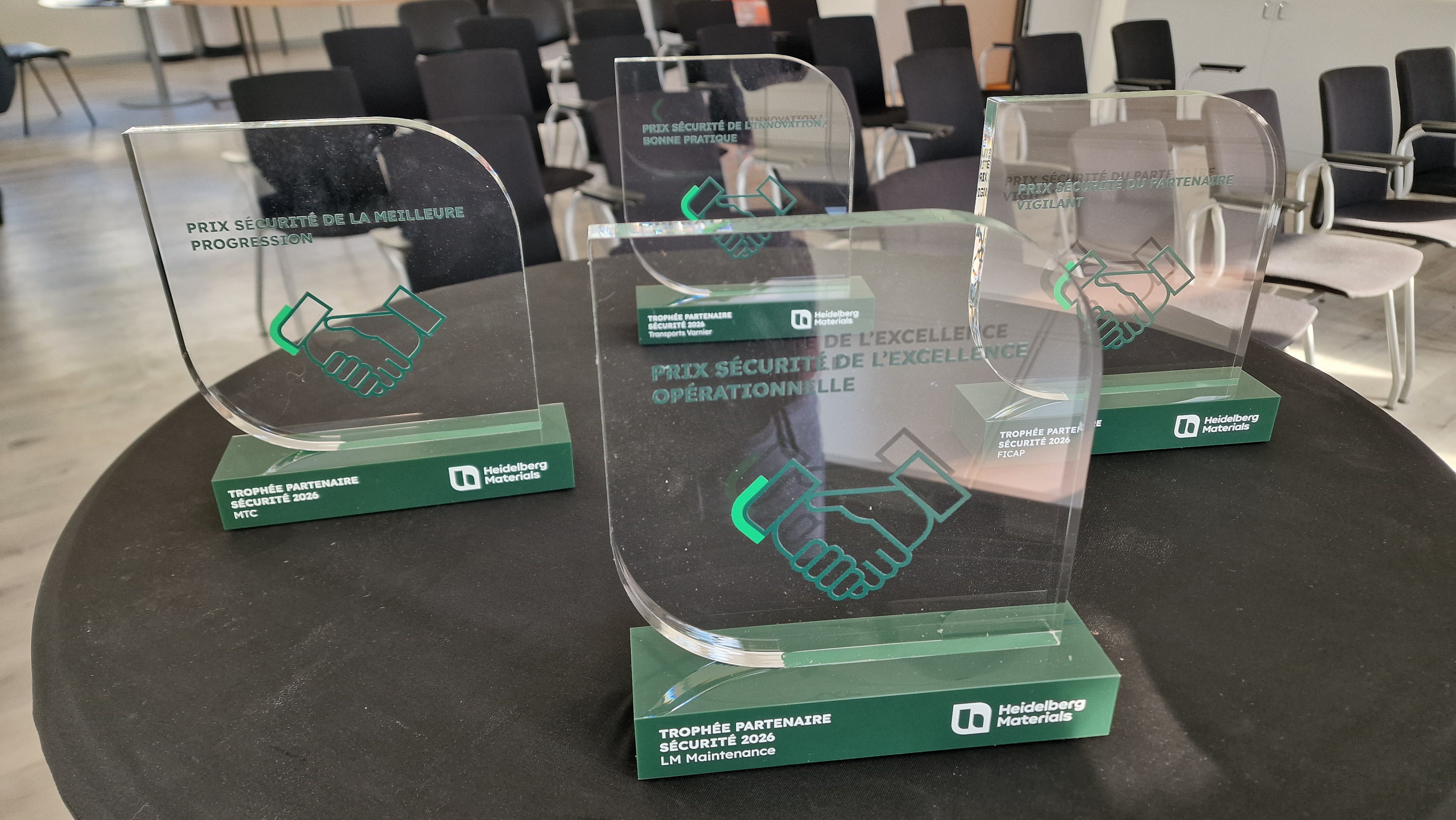 Trophées en verre gravés avec un symbole de poignée de main, posés sur une table dans une salle de conférence.