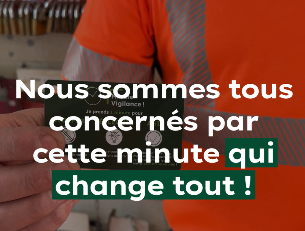 A person in a high-visibility orange shirt holds a card with safety-related text in French.