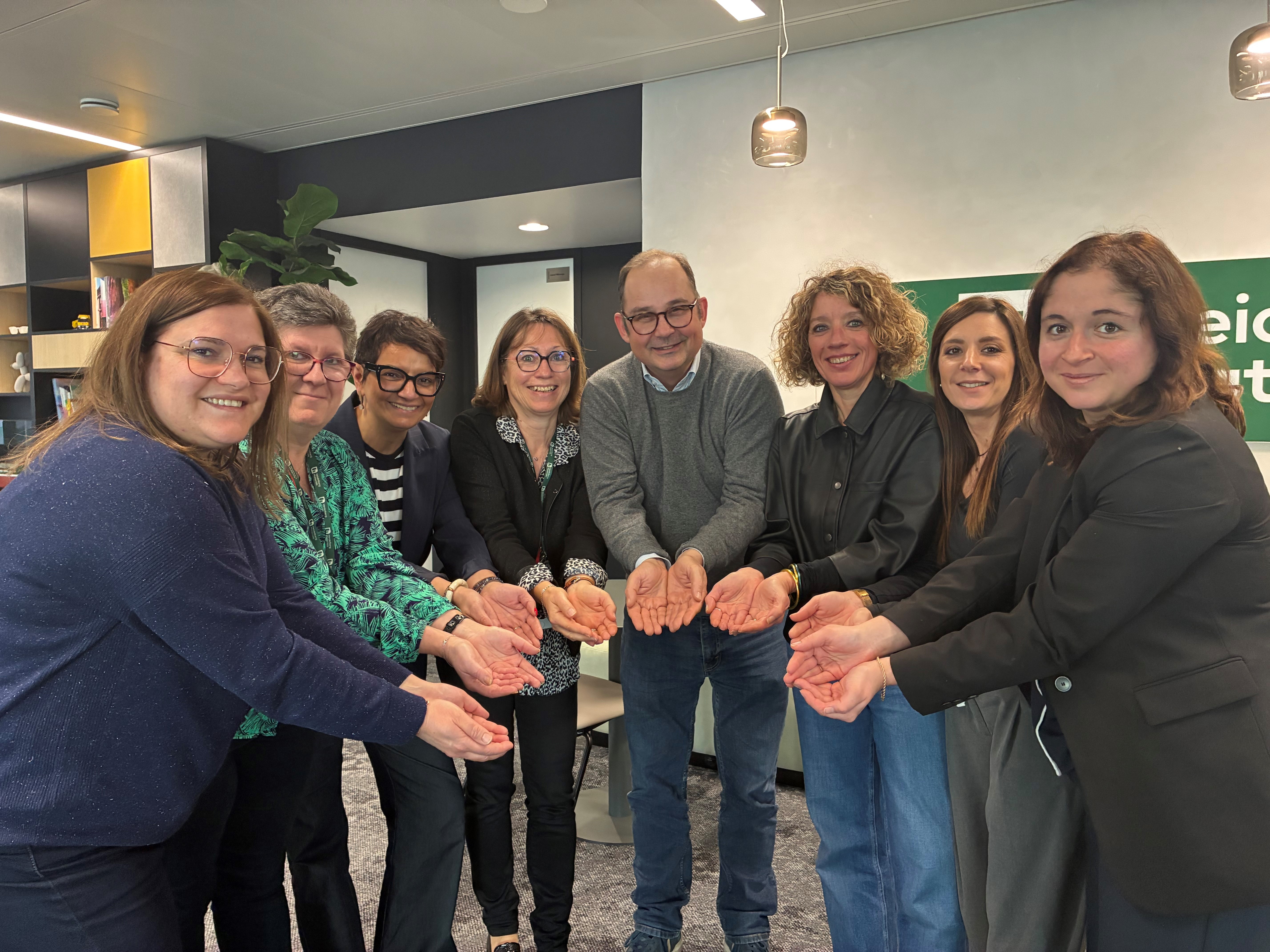 Des employés souriants de Heidelberg Materials réunis dans un cadre professionnel, en train de faire le geste #GivetoGain avec les mains.