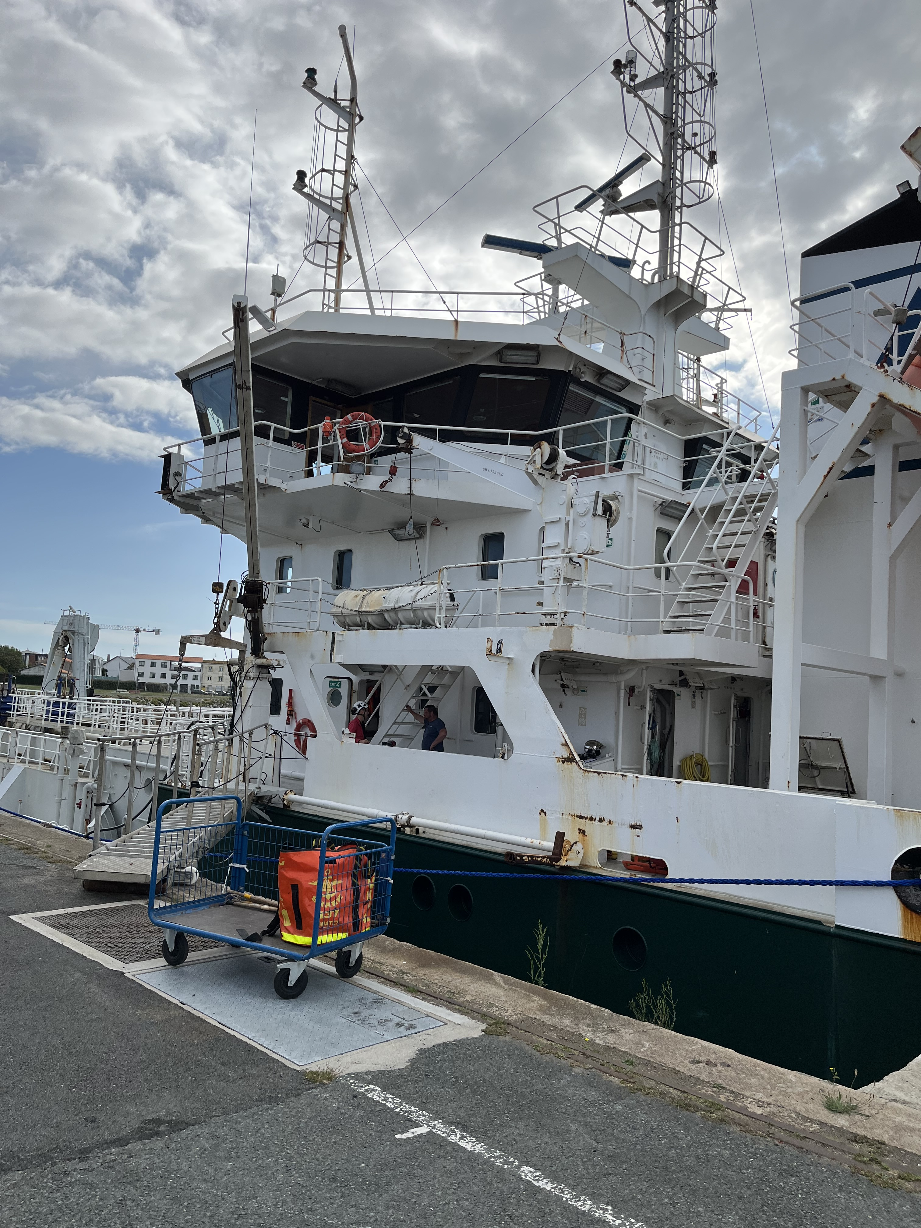 Un bateau industriel blanc est amarré au port sous un ciel partiellement nuageux.