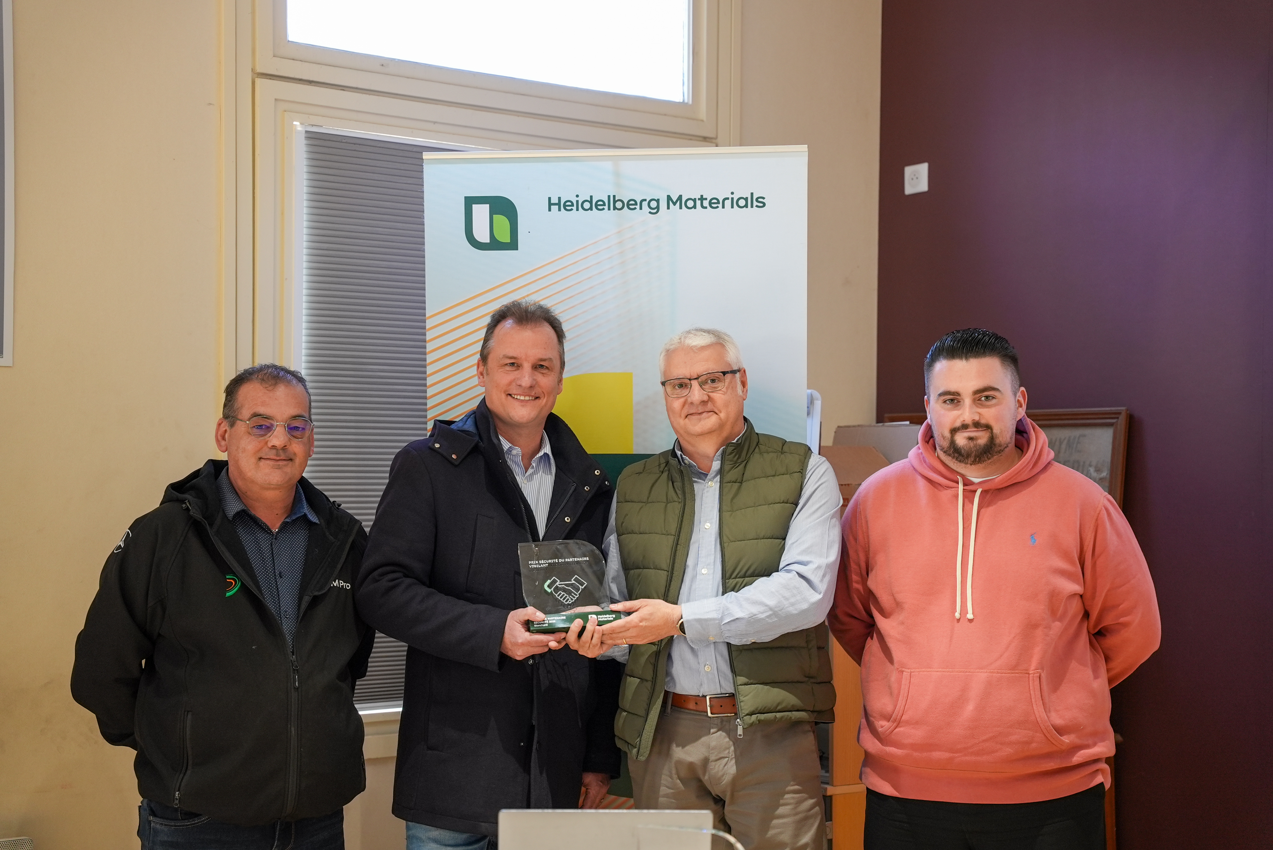 Quatre personnes posent avec un trophée devant un panneau de Heidelberg Materials.