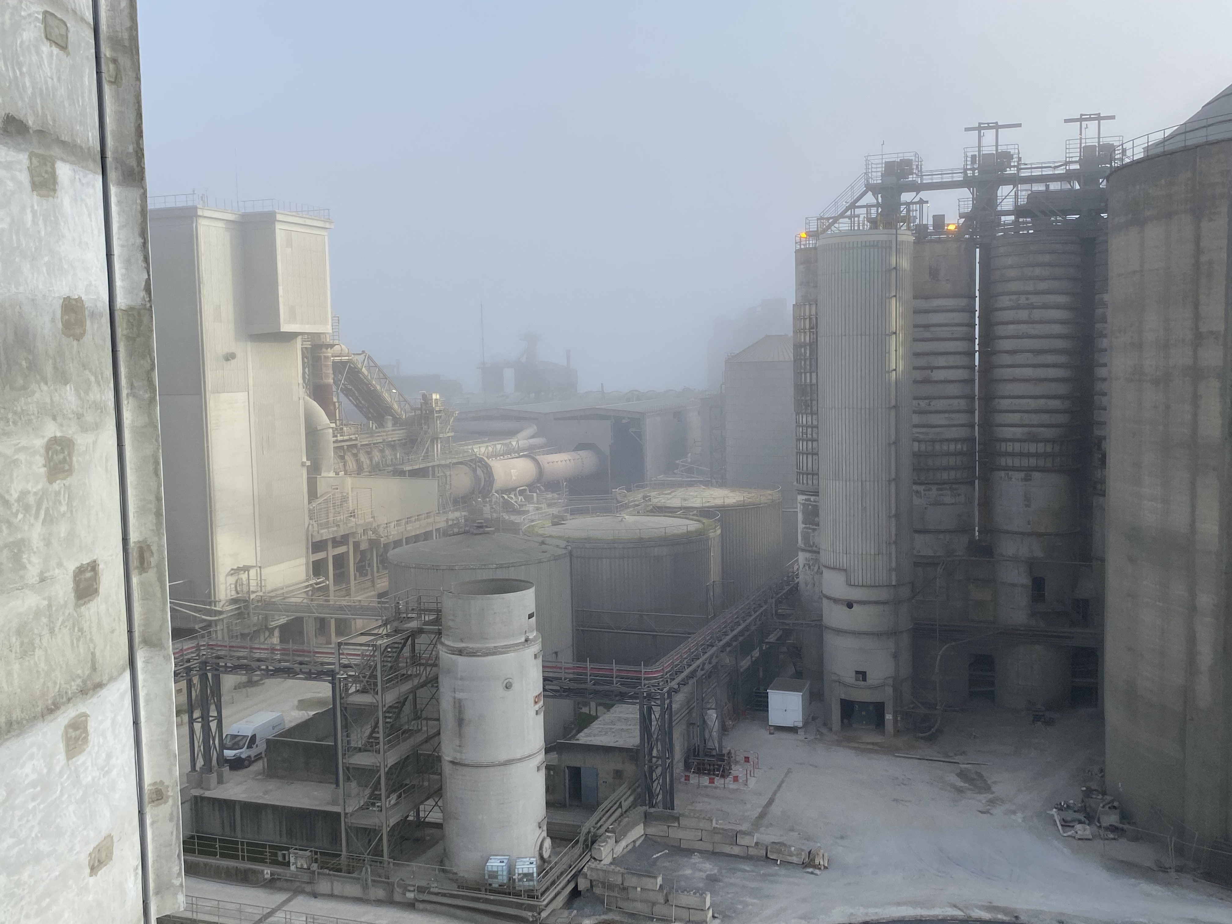 Site industriel avec des silos et des équipements de production de matériaux de construction dans une ambiance brumeuse.