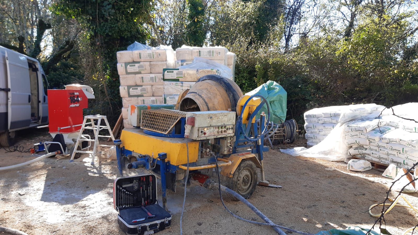 Bétonnière sur un chantier avec des sacs de ciment empilés en arrière-plan.
