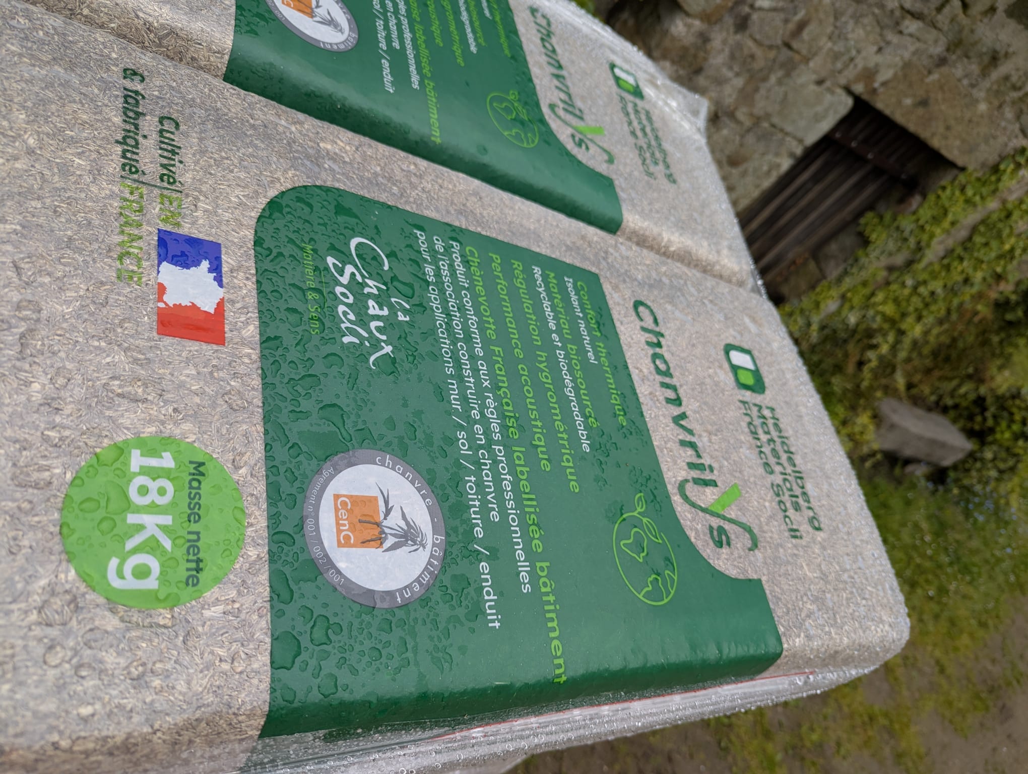 Sacs de matériau de construction en chanvre posés à l'extérieur, étiquetés avec des informations sur le poids et la provenance.