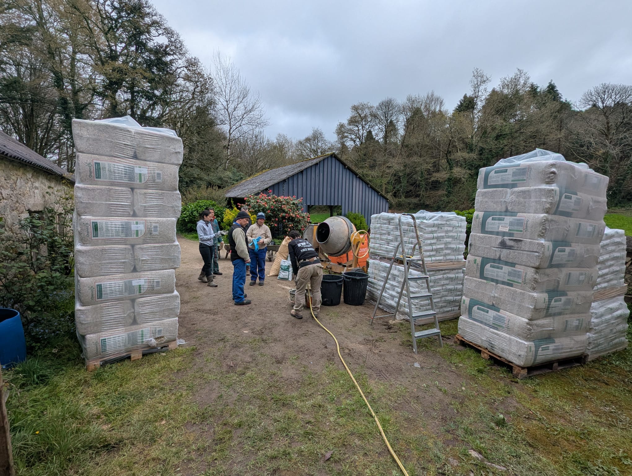 Des employés travaillant sur un site avec des piles de sacs de matériaux de construction et une bétonnière au centre.