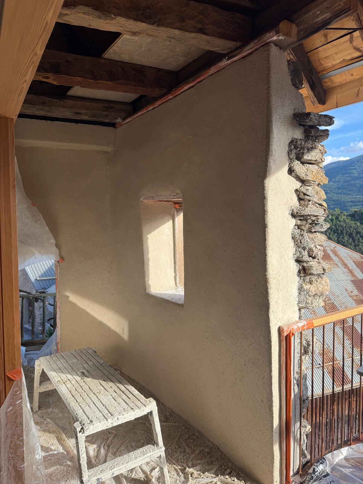 Un mur en construction avec une ouverture pour une fenêtre, dans un environnement rural ensoleillé.