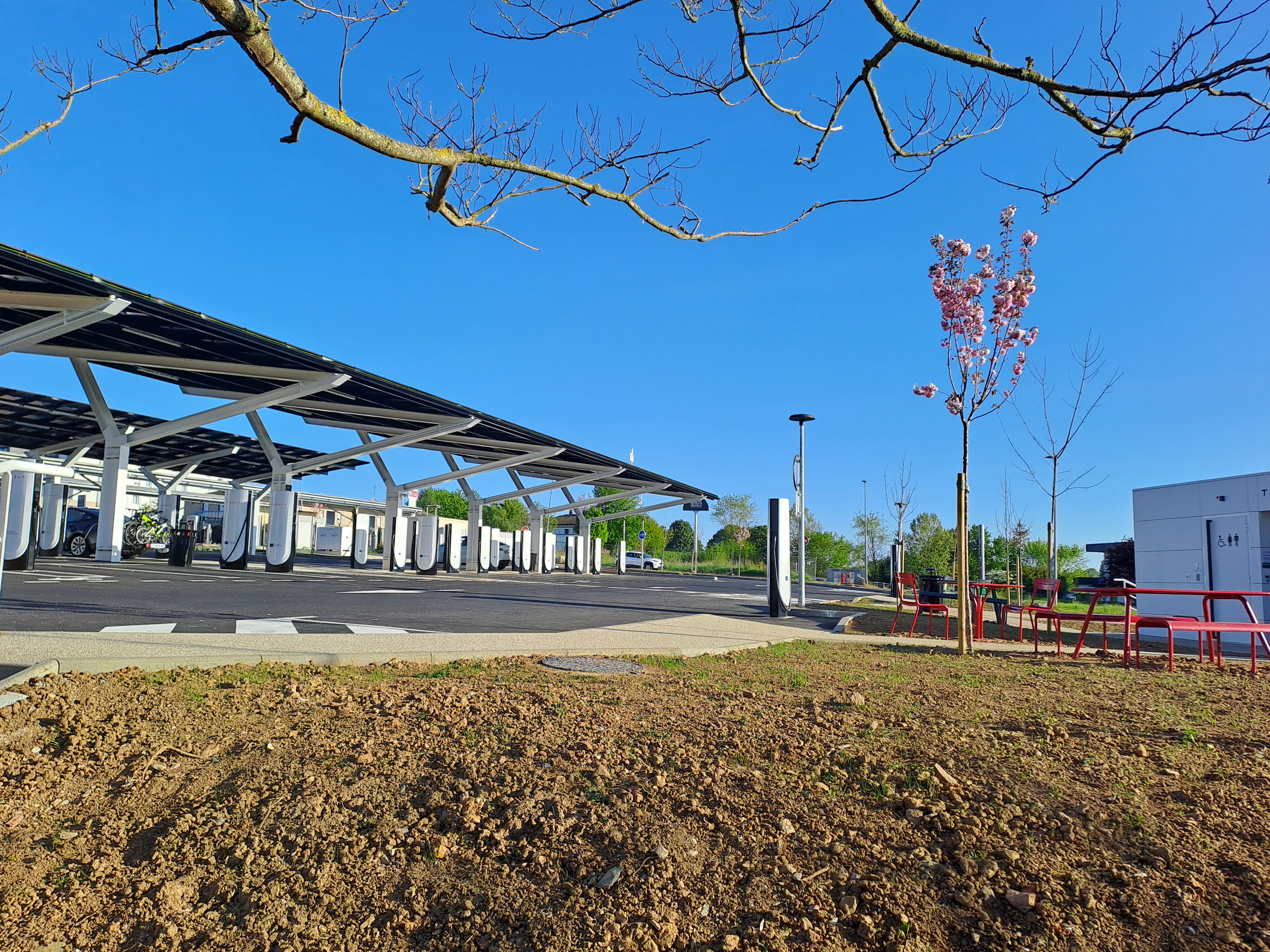 Site industriel avec des bornes de recharge pour véhicules électriques sous des auvents solaires.