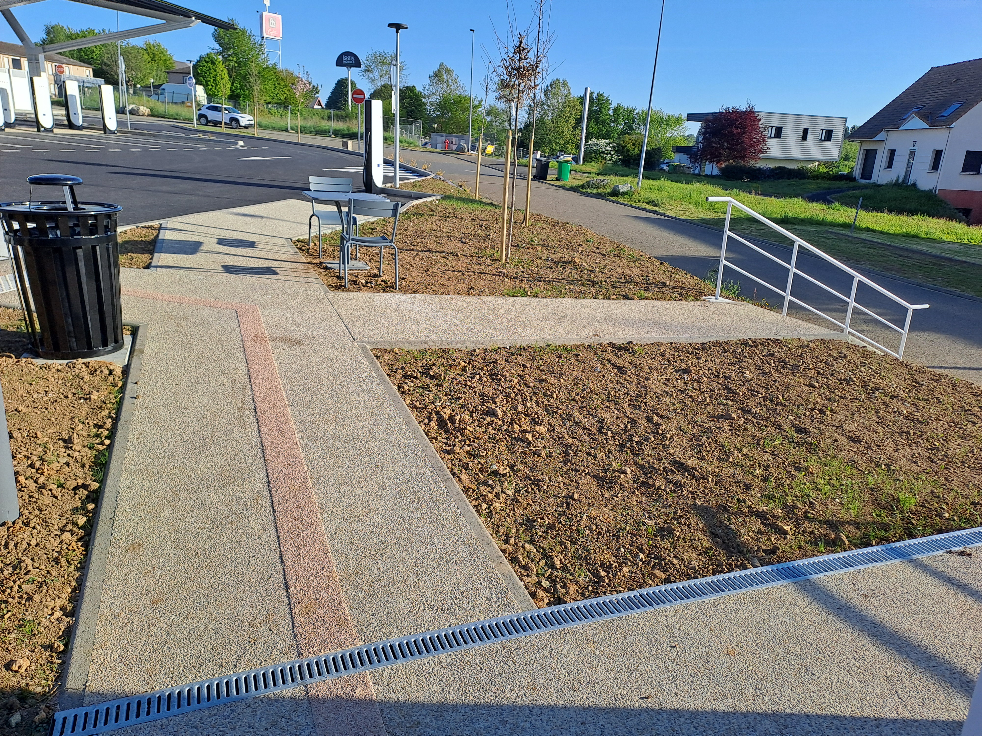 Cheminements en béton dans un espace public avec des plates-bandes de terre et des jeunes arbres récemment plantés.
