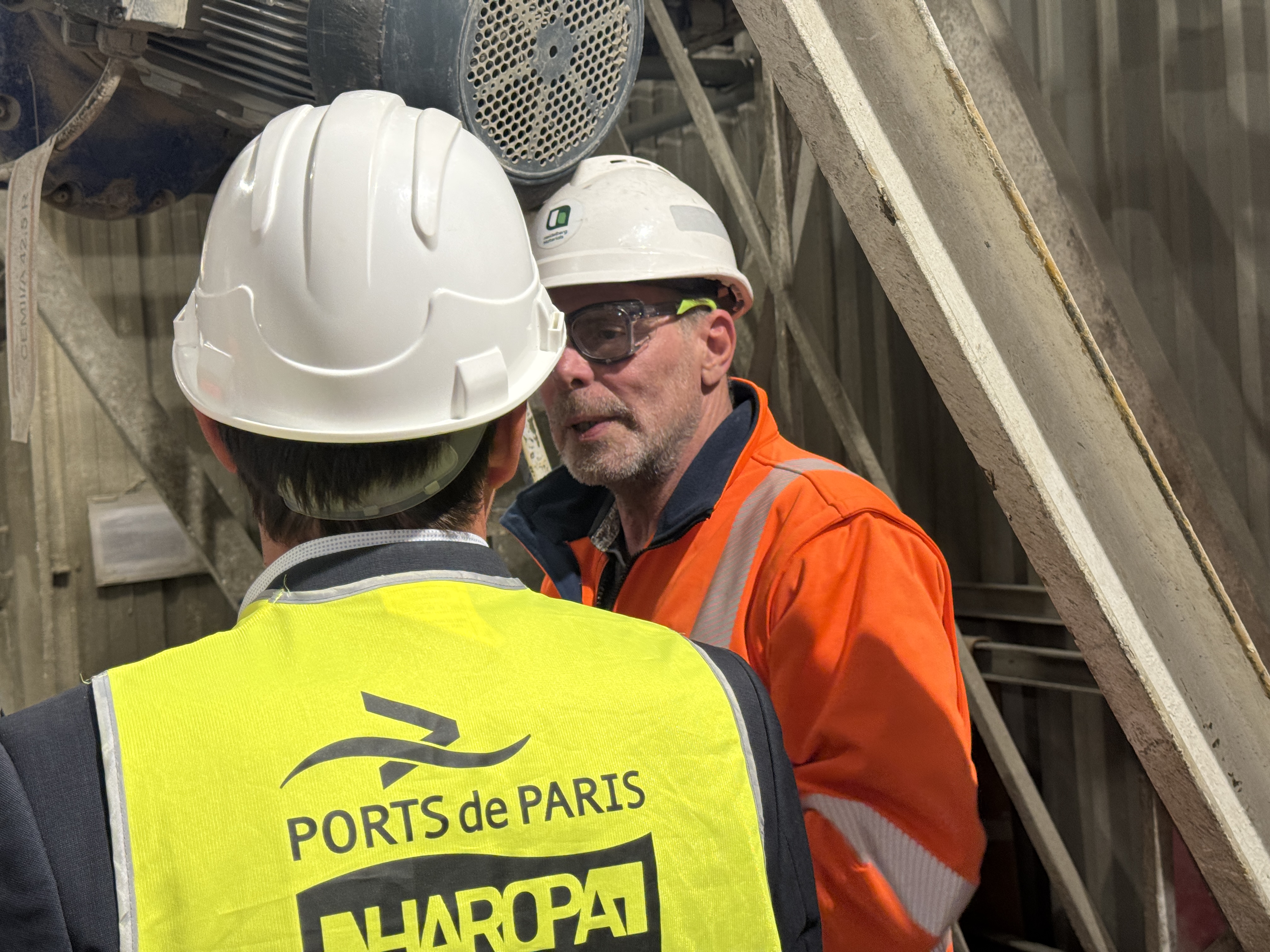 Deux personnes en tenue de sécurité discutent sur un site industriel.
