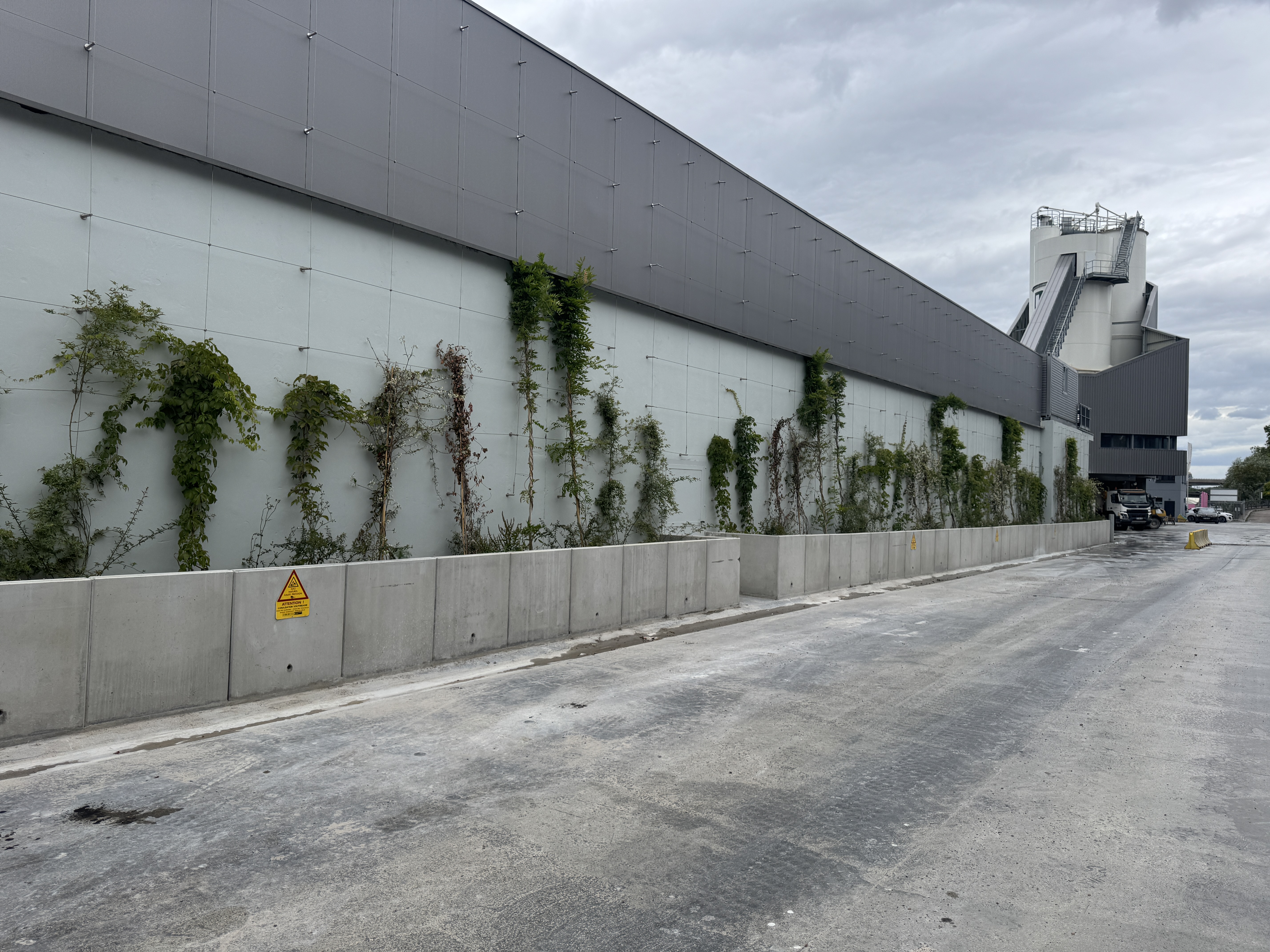 Bâtiment industriel avec façade grise recouverte partiellement de végétation grimpante.