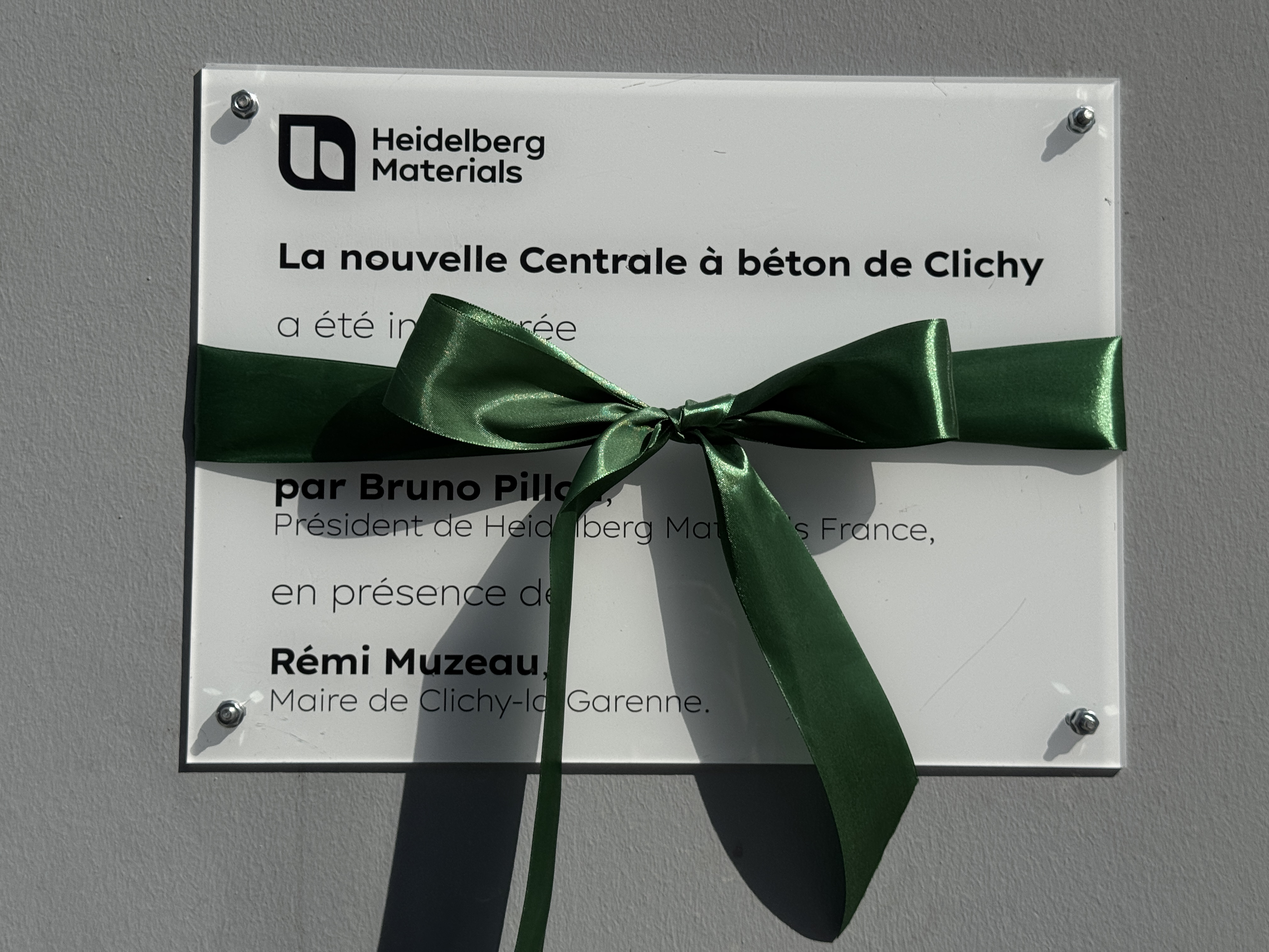 Plaque inaugurale de la nouvelle centrale à béton à Clichy ornée d'un ruban vert.