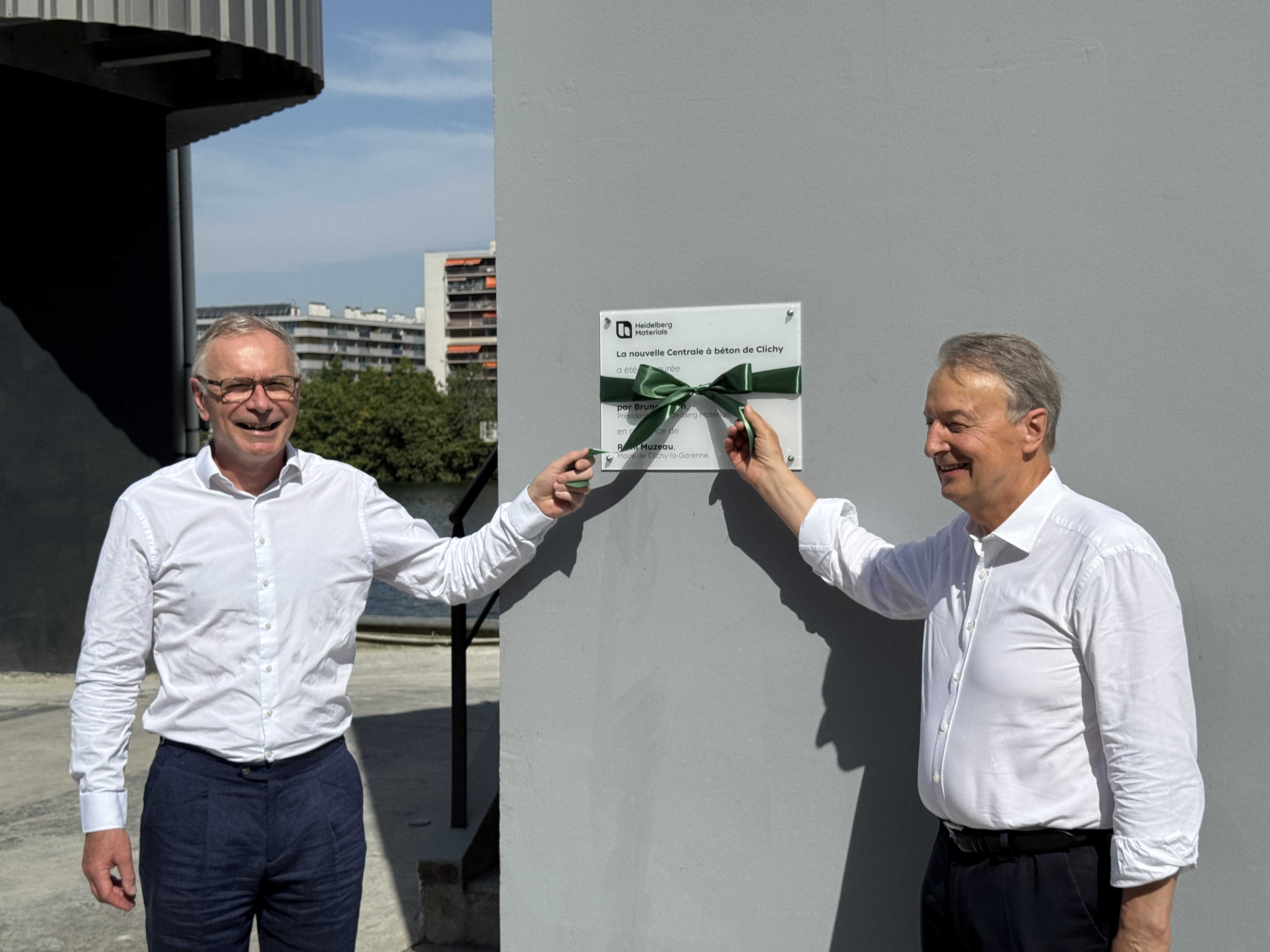 Deux hommes inaugurent une plaque sur un site industriel, tenant un ruban vert.