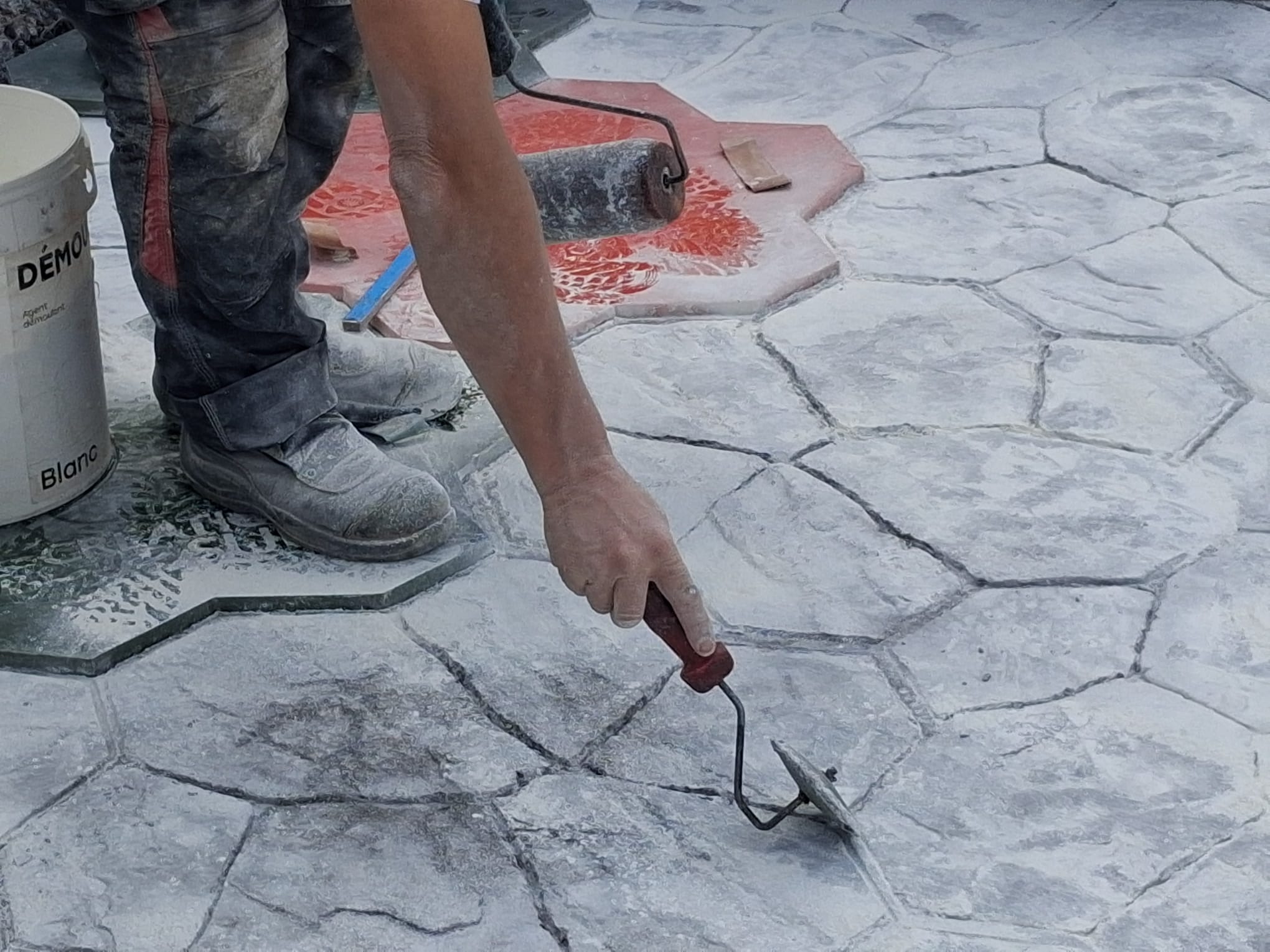 Un ouvrier applique une finition sur une surface en béton estampé.