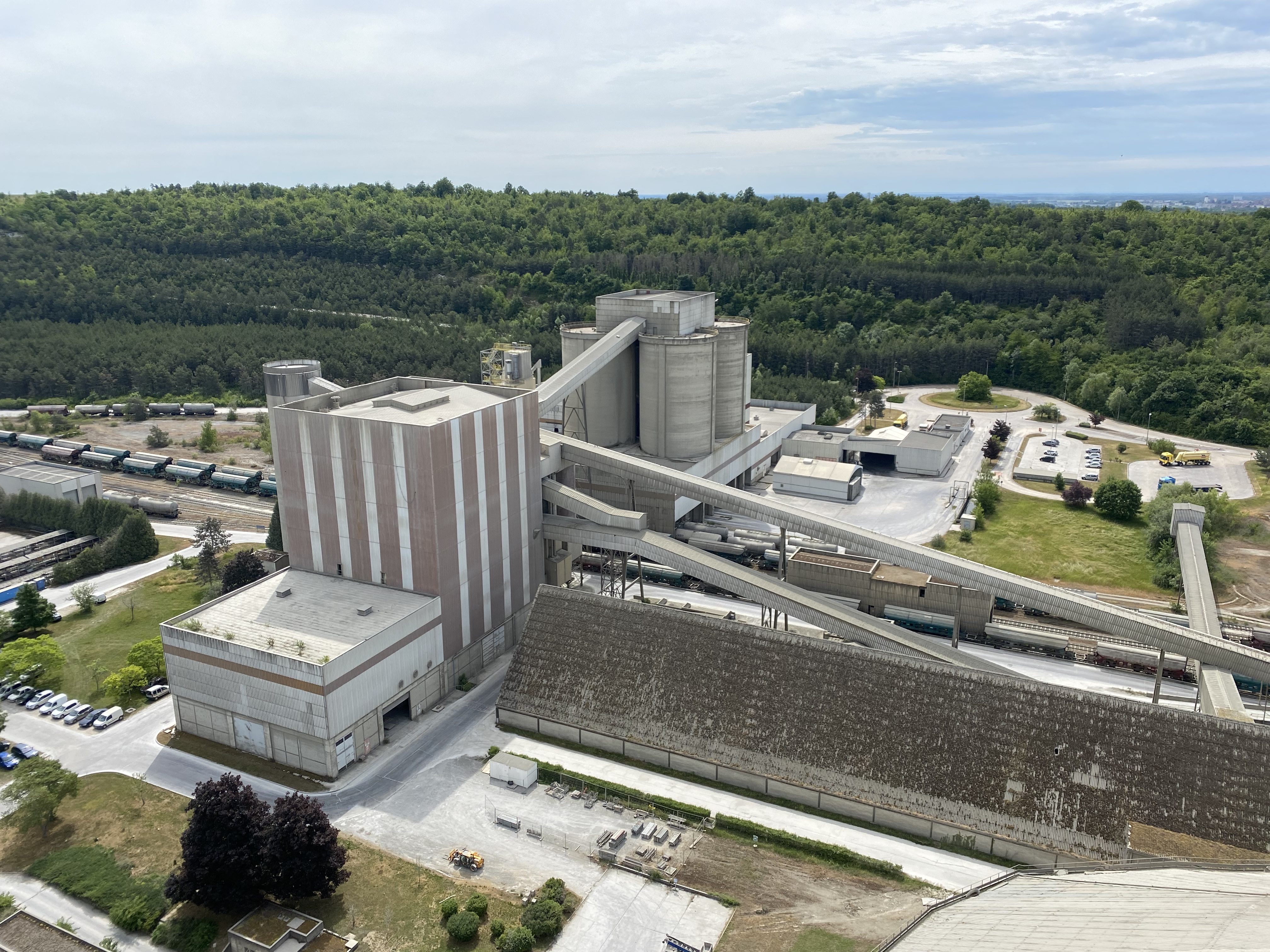 Site industriel avec plusieurs bâtiments et zones de stockage, entouré de végétation.