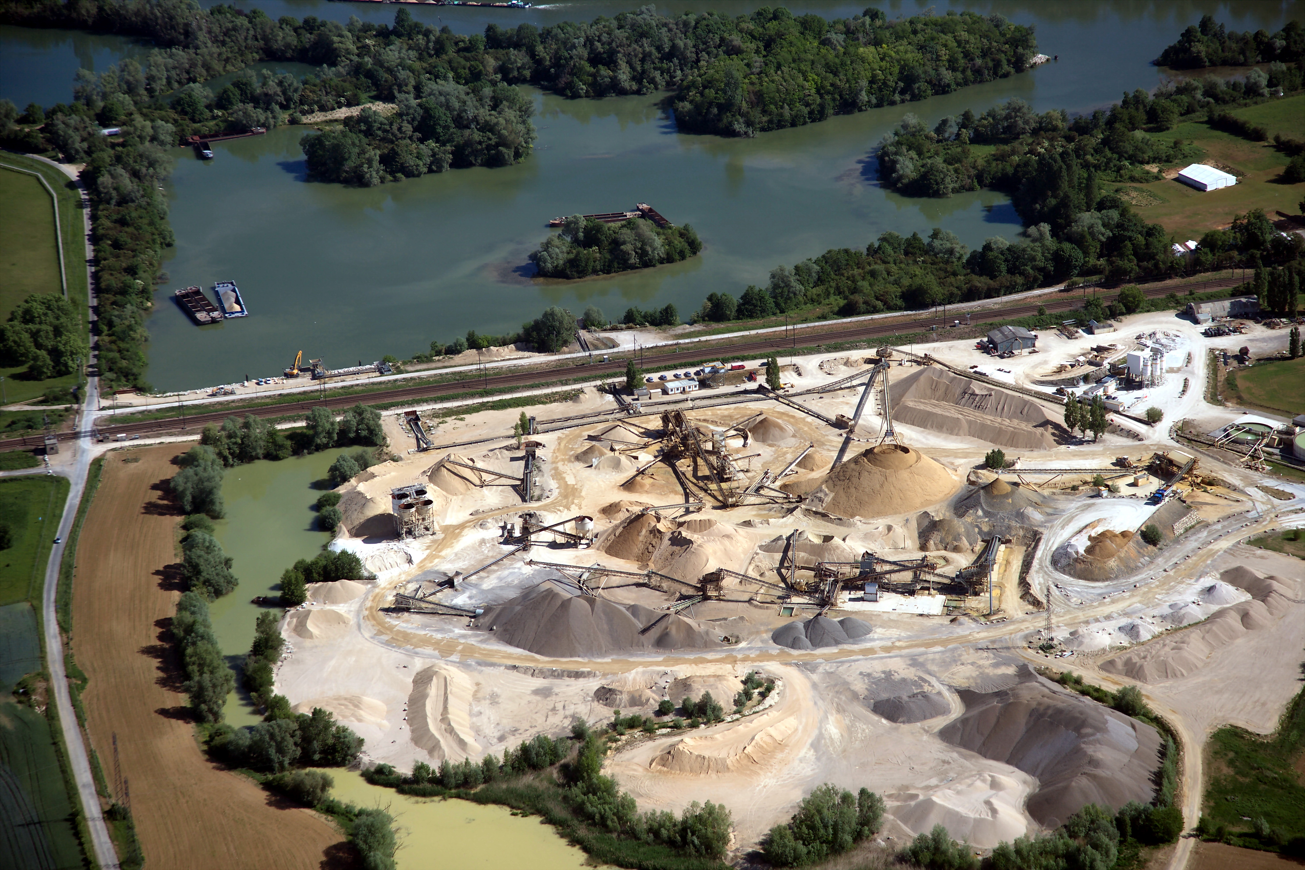 Site industriel de production de matériaux de construction entouré de végétation et de plans d'eau.