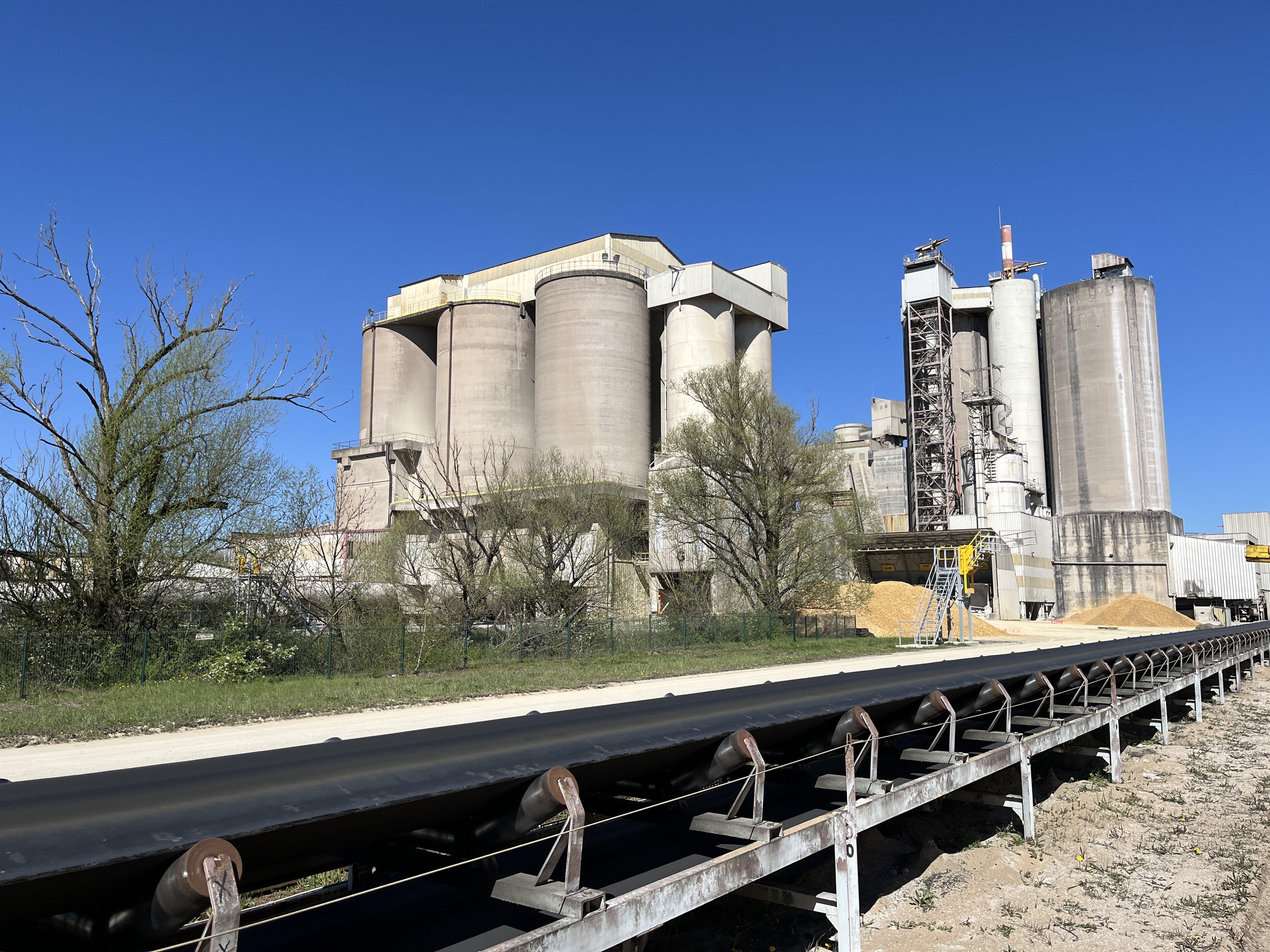 Site industriel avec des silos de stockage et un tapis roulant au premier plan.