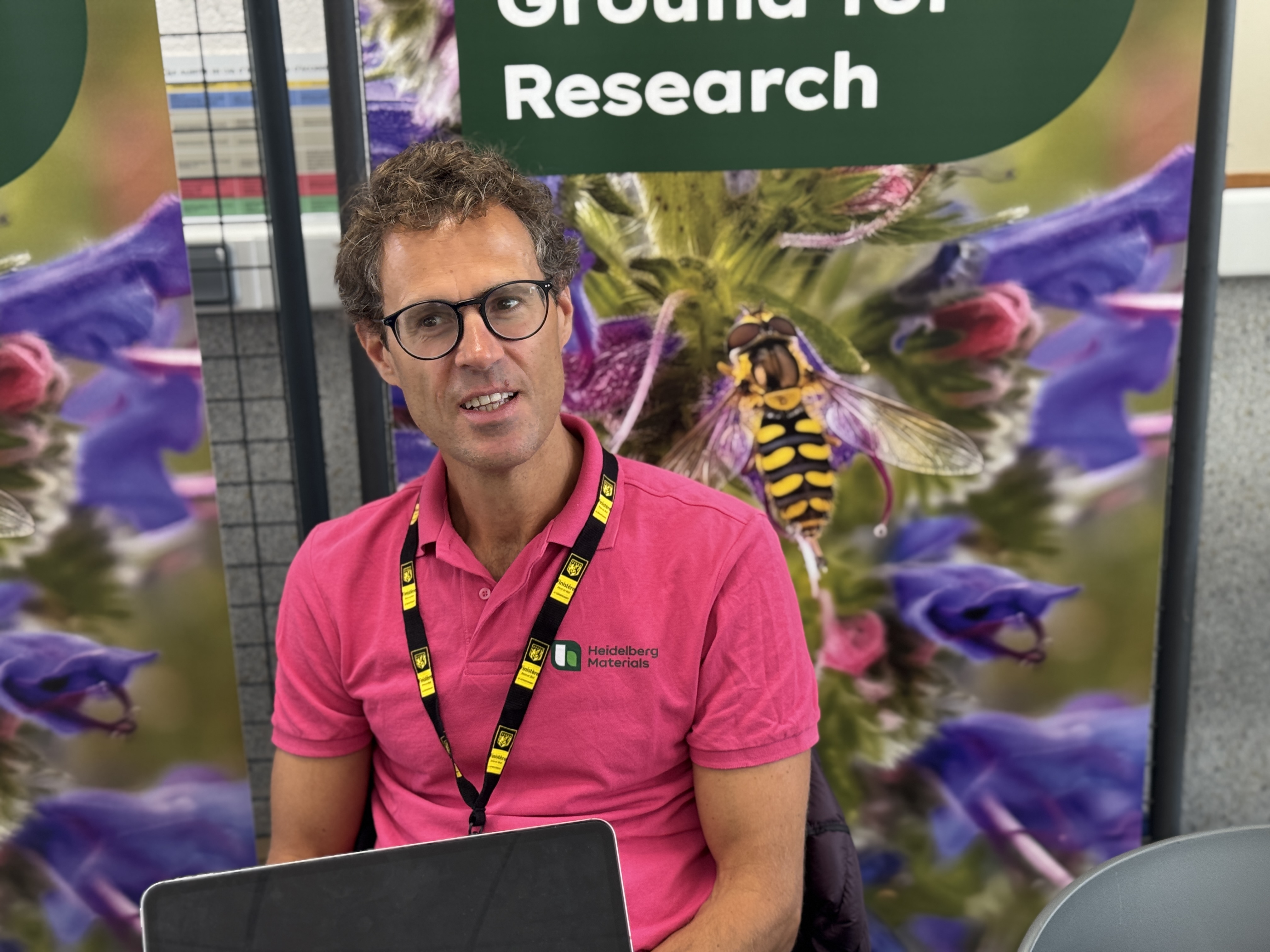 Une personne assise devant un stand promotionnel sur la recherche, avec des panneaux illustrant des fleurs et des insectes.