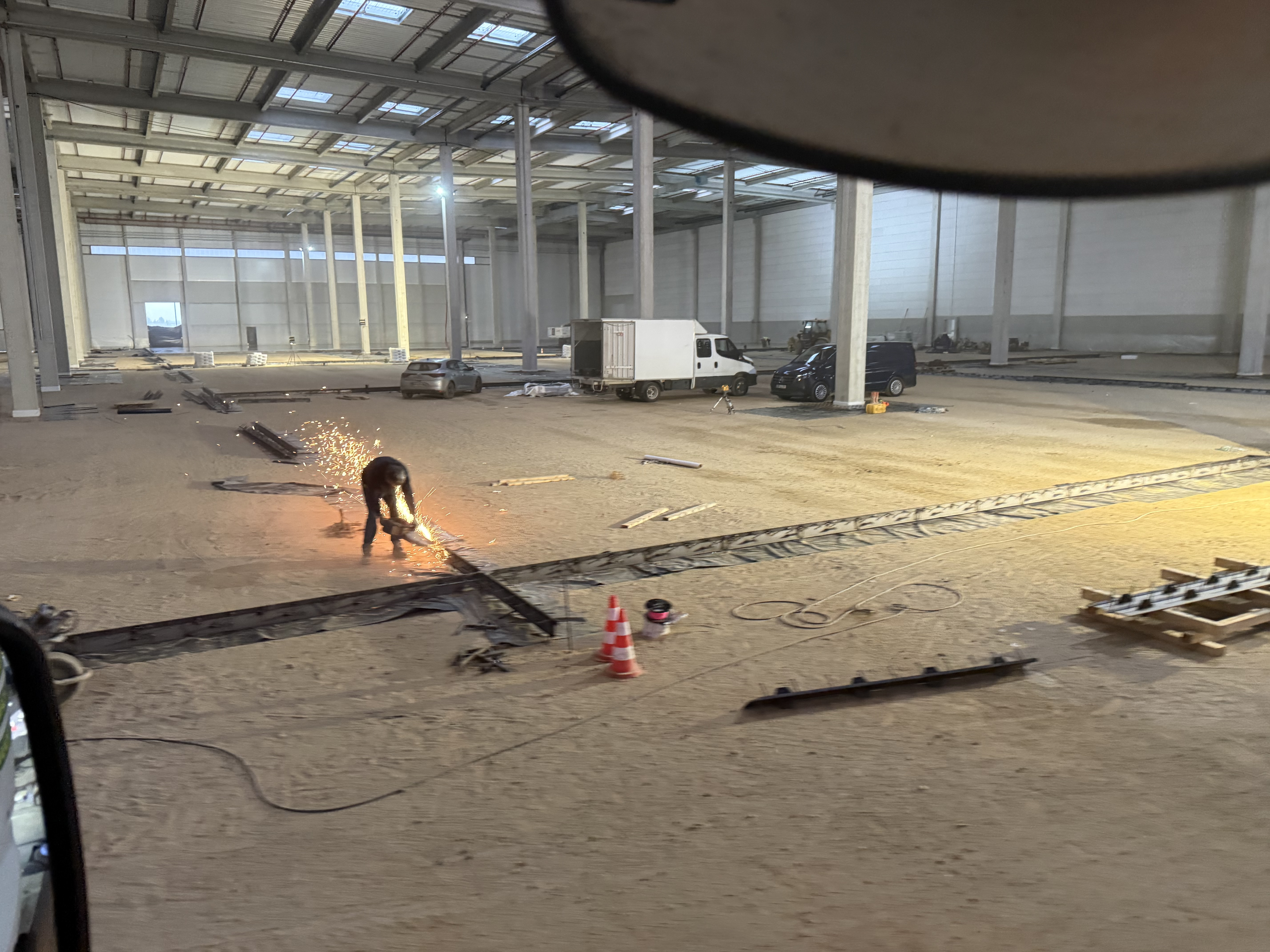 Vue intérieure du futur centre logistique CULTURA en construction à Ferrières-en-Gâtinais. Un opérateur réalise des travaux de découpe métallique dans un vaste espace industriel équipé de poteaux structurels et préparé pour la mise en œuvre des dallages en béton.