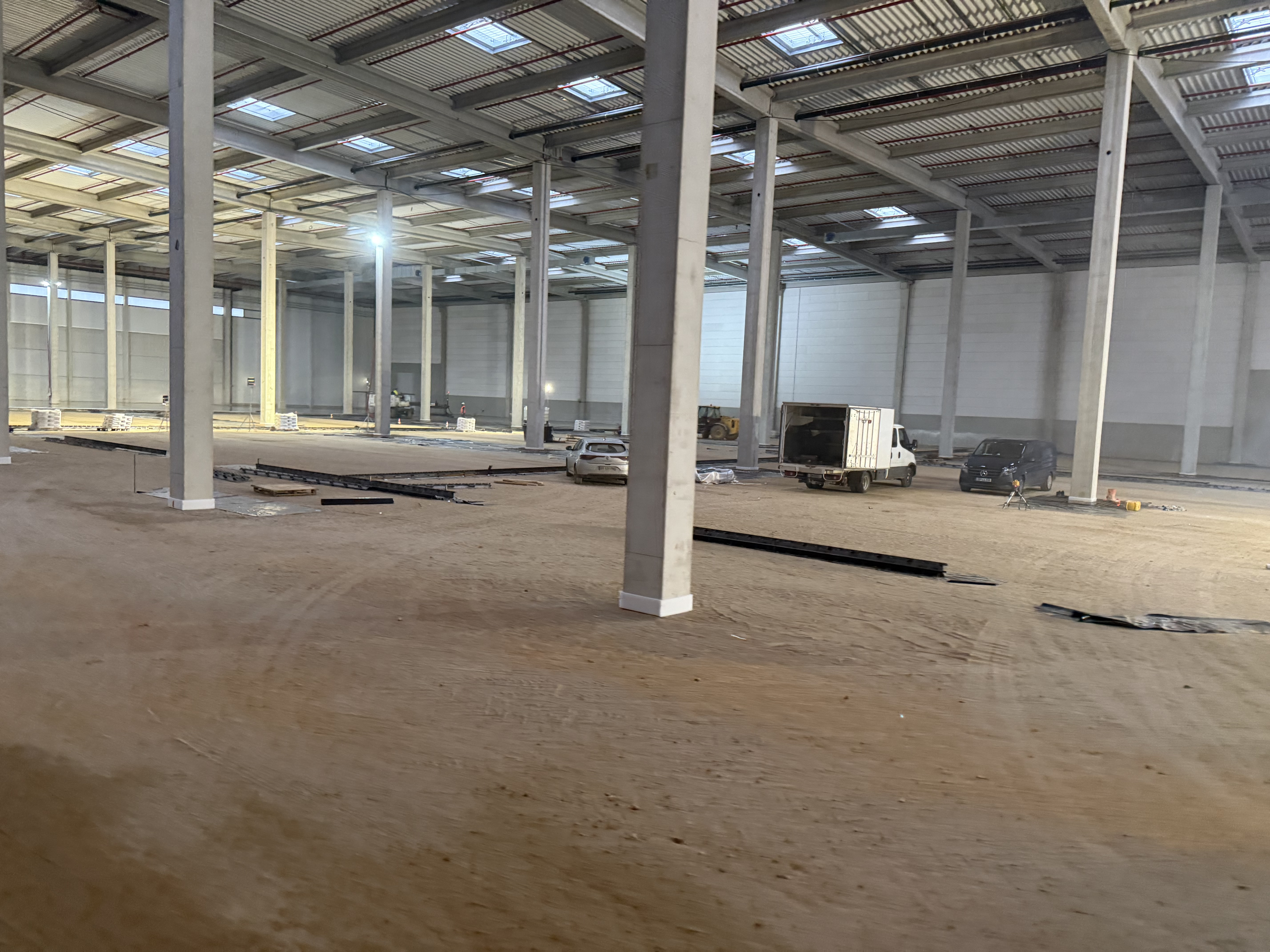 Un grand espace industriel en construction avec un sol en terre battue et quelques équipements dispersés.