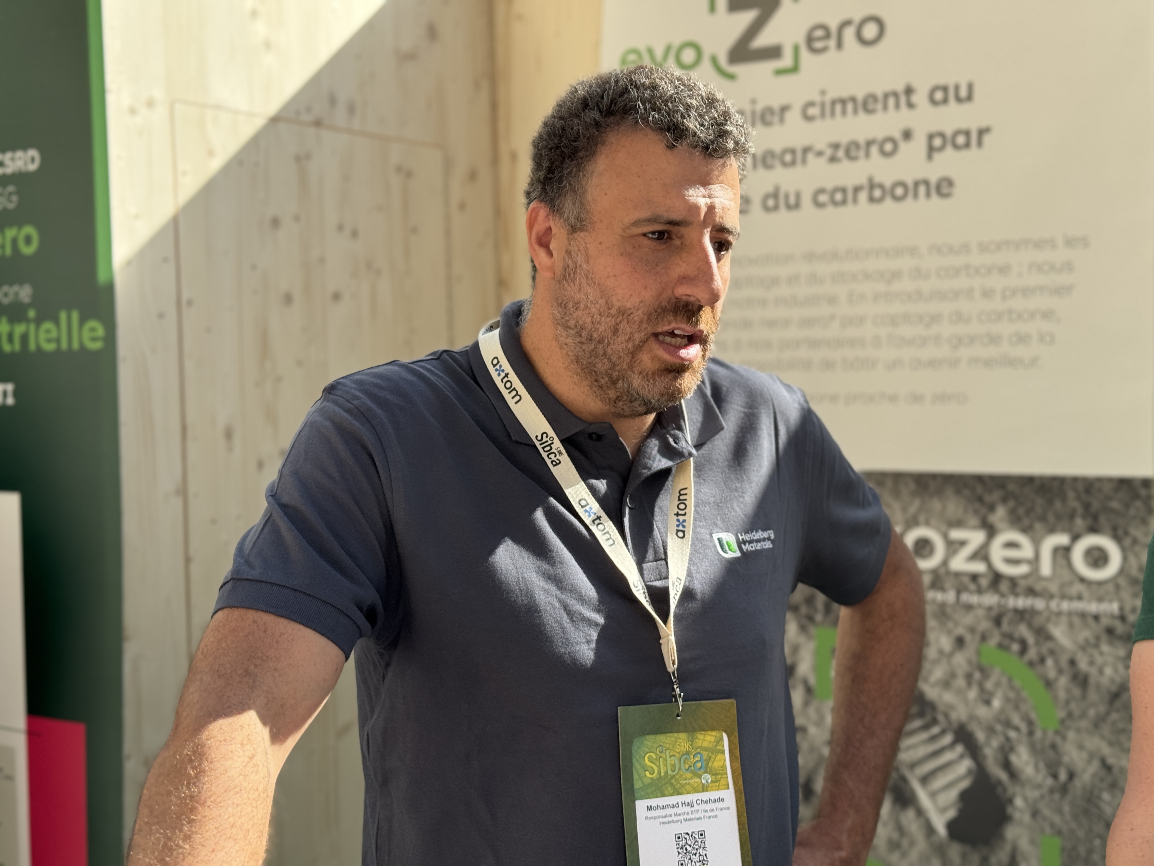 Un homme se tient devant une bannière présentant des informations sur le ciment à faible empreinte carbone.