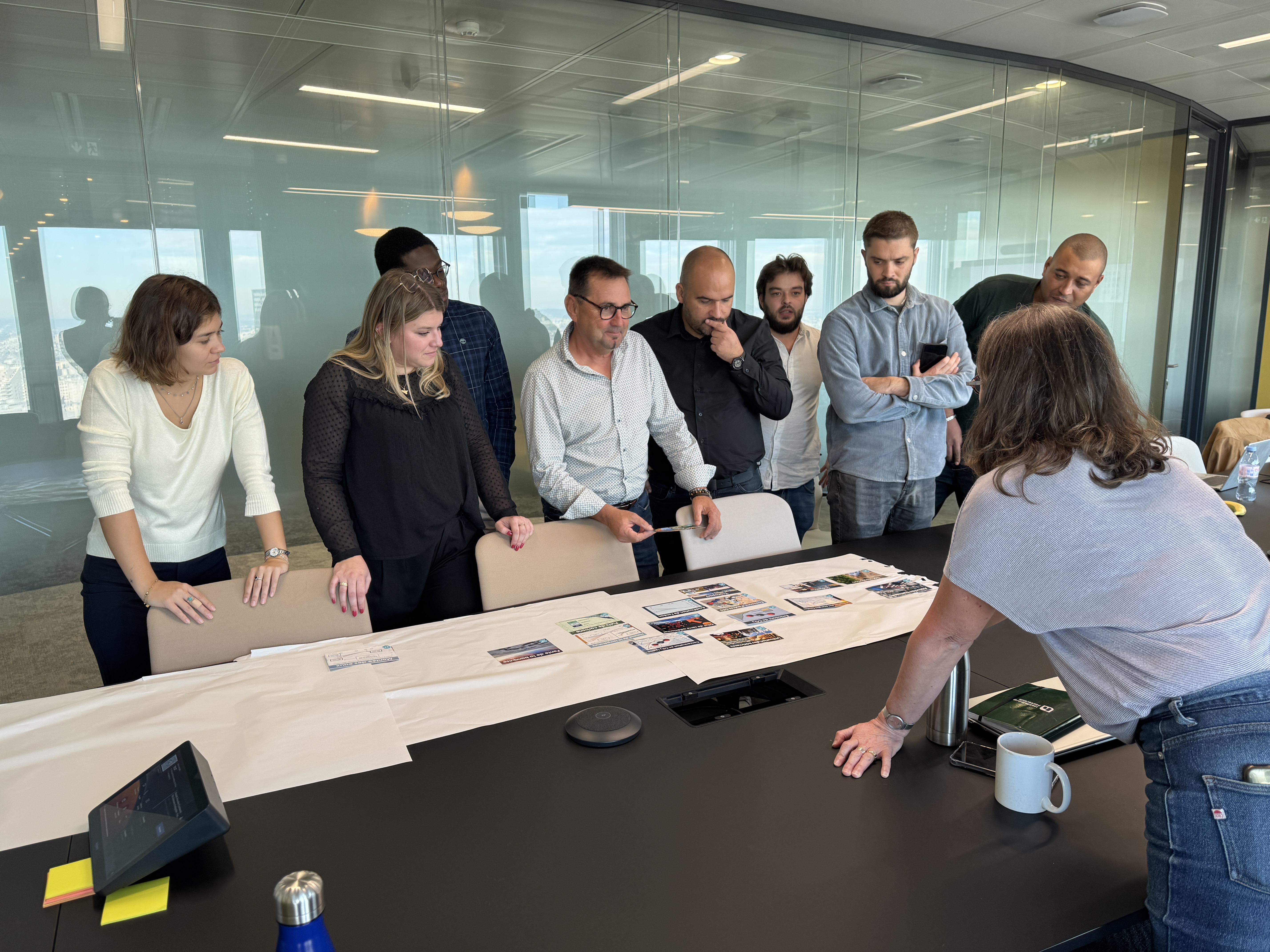 Des collaborateurs discutent autour d'une table avec des documents étalés dans une salle de réunion.